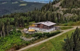 Luftaufnahme einer Bergh&uuml;tte inmitten von Wald und Bergen.
