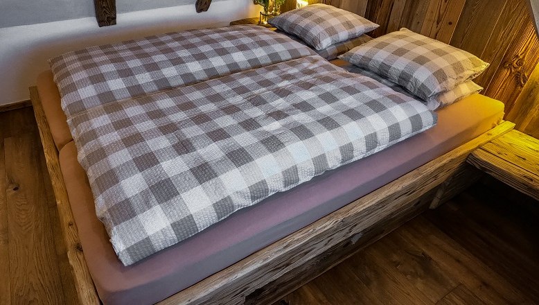 Gem&uuml;tliches Bett mit kariertem Bettzeug in einer Holzh&uuml;tte.