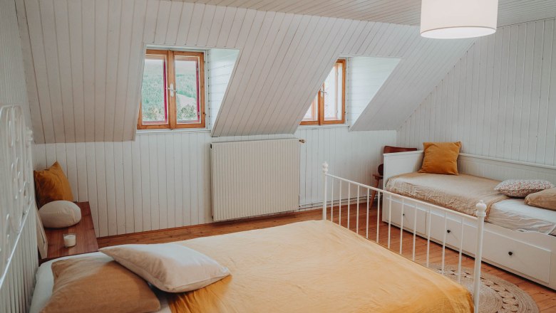 Gemütliches Schlafzimmer mit zwei Betten, Holzboden und Dachfenstern.