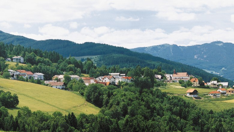 Panorama von St. Corona am Wechsel mit gr&uuml;nen H&uuml;geln und Bergen im Hintergrund.