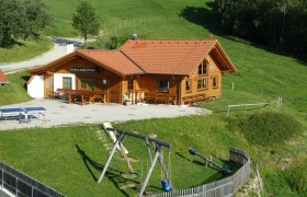 Eine Berghütte namens Simashütte mit rotem Dach, umgeben von grünen Wiesen und einem Spielplatz mit Schaukel.
