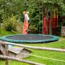 Ein Kind springt auf einem Trampolin in einem Garten mit Rutsche und Spielhaus.