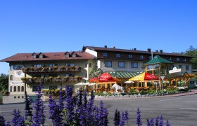 Gasthof Ramswirt mit bl&uuml;henden Balkonen und Sonnenschirmen vor blauem Himmel.