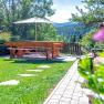 Garten mit Holztisch, Bänken und Sonnenschirm, umgeben von Bäumen und Wiese.