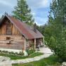 Eine rustikale Holzhütte mit rotem Dach in einer bewaldeten Umgebung, umgeben von Bäumen und einem gepflegten Garten.