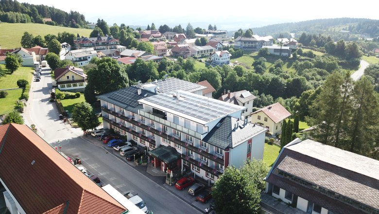Luftaufnahme eines Hotels mit Solarpanelen auf dem Dach, umgeben von B&auml;umen und weiteren Geb&auml;uden in einer l&auml;ndlichen Gegend.