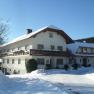 Ein großes Bauernhaus im Winter mit Schnee bedeckt, unter blauem Himmel.