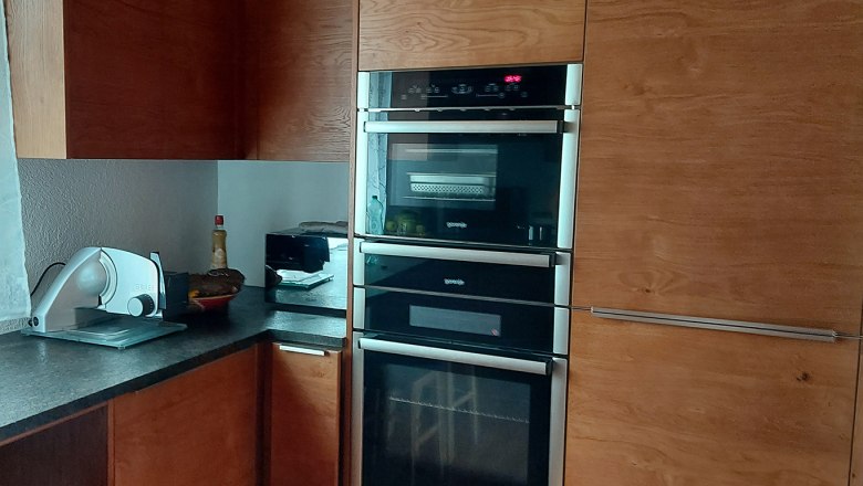 Moderne Küche mit Holzschränken, eingebautem Ofen und Arbeitsplatte mit Küchengeräten.