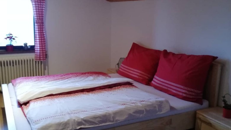 Gemütliches Schlafzimmer mit Holzbett, roten Kissen und karierten Vorhängen unter einer Holzdecke.
