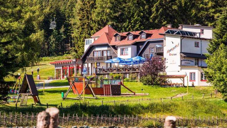 Alpengasthof Enzian mit Spielplatz und Wald im Hintergrund.