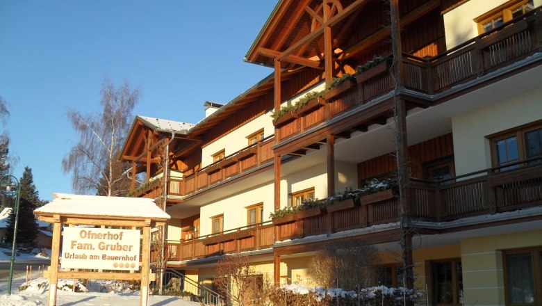 Ein traditionelles Bauernhaus mit Holzverkleidung im Winter, beschriftet mit 'Ofnerhof Fam. Gruber'.
