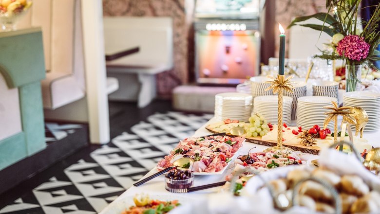 Ein reichhaltiges Buffet mit verschiedenen Speisen, Geschirrstapeln und dekorativen Kerzenhaltern in einem stilvollen Raum.