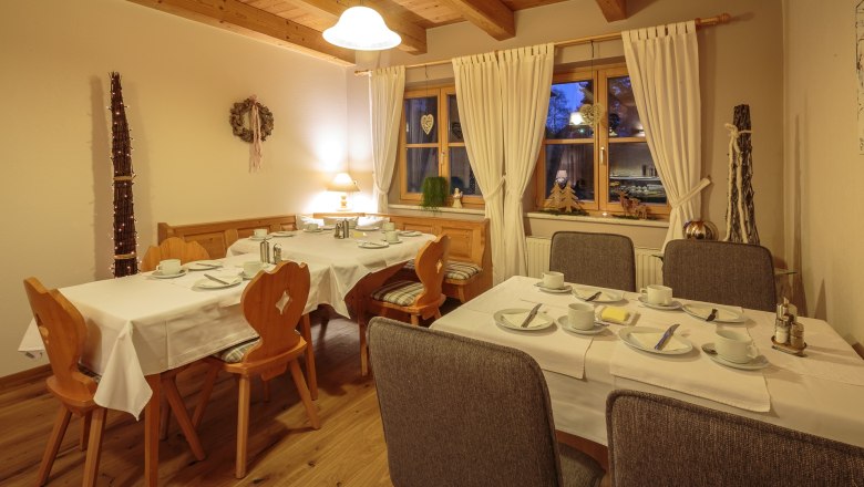 Gemütlicher Frühstücksraum mit gedeckten Tischen, Holzmöbeln und Dekorationen.