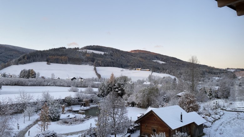 Winterlandschaft mit schneebedeckten Hügeln und einem Holzhaus im Vordergrund.