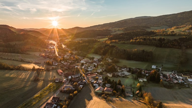Luftaufnahme eines Dorfes in einer h&uuml;geligen Landschaft bei Sonnenuntergang.