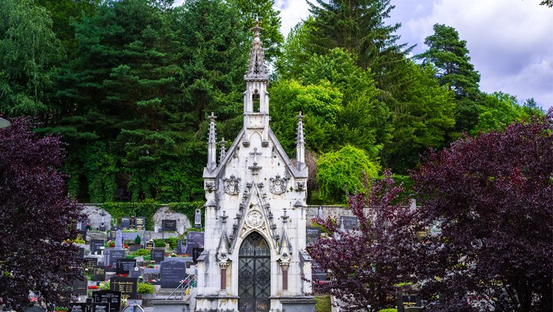 Eine gotische Grabkapelle auf einem Friedhof, umgeben von Bäumen und Grabsteinen.