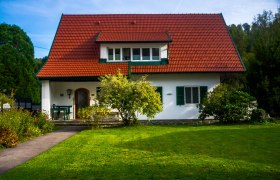Ein weißes Haus mit rotem Dach und grünem Fensterladen, umgeben von einem gepflegten Garten.