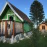 Zwei kleine Holzh&uuml;tten im Glamping-Stil mit gr&uuml;ner und brauner Fassade, umgeben von B&auml;umen und Gras.