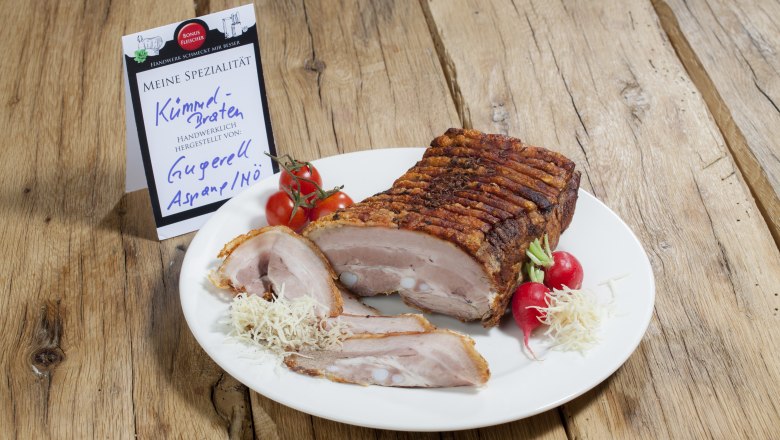 Ein Teller mit K&uuml;mmelbraten, Radieschen und Tomaten auf einem Holztisch.