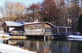 Ein Restaurant am Ufer eines Teiches im Winter, umgeben von Bäumen.