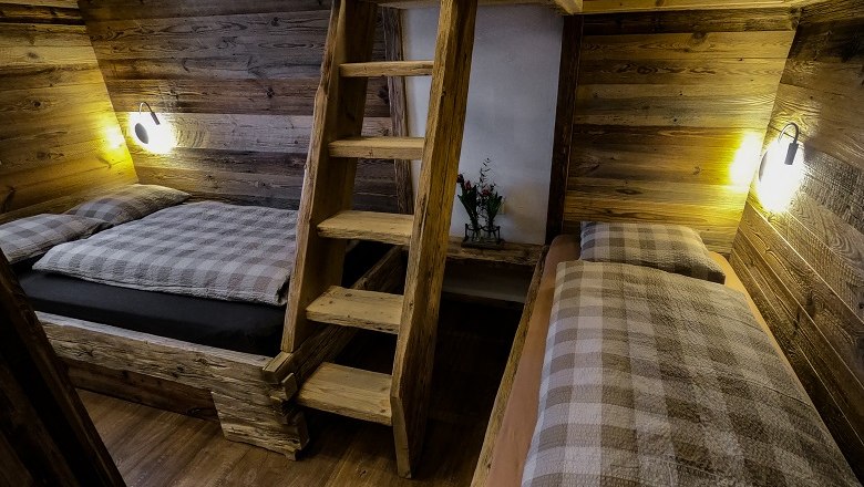 Innenansicht einer rustikalen Holzhütte mit zwei Betten und einer Holzleiter.