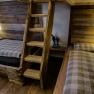 Innenansicht einer rustikalen Holzhütte mit zwei Betten und einer Holzleiter.
