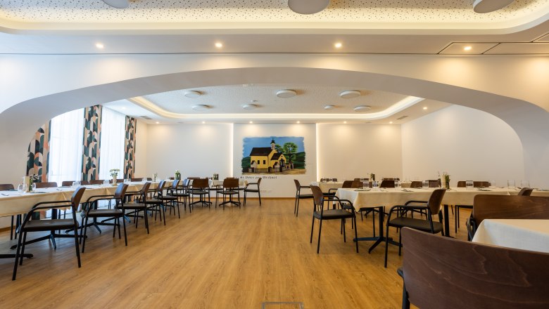 Innenansicht eines modernen Wirtshauses mit gedeckten Tischen und einem Wandgemälde.