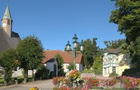 Hauptplatz in M&ouml;nichkirchen mit Kirche, Blumen und historischen Geb&auml;uden.