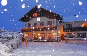 Ein beleuchtetes Bauernhaus im Schnee bei Nacht.