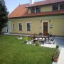 Ein gelbes Haus mit rotem Dach und Terrasse, umgeben von Rasen und Pflanzen.