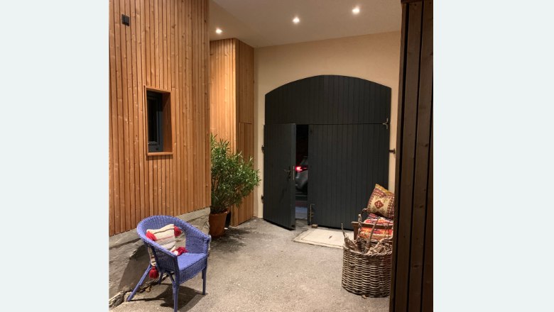 Ein Innenhof mit Holzwänden, einem blauen Stuhl, einer Pflanze und einem großen schwarzen Tor.