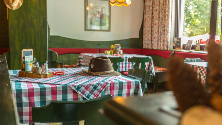 Gemütliche Gaststube mit karierten Tischdecken und einem Hut auf dem Tisch.