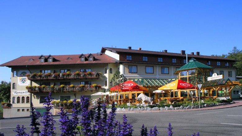 Gasthof Ramswirt mit bl&uuml;henden Balkonen und Sonnenschirmen vor blauem Himmel.