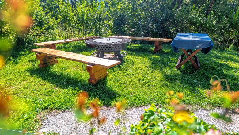 Ein Grillplatz mit Holzbänken und einem Tisch im Freien, umgeben von grüner Vegetation.