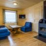 Gemütliches Wohnzimmer mit Holzwänden, blauen Sofas, Holztisch und Kaminofen.