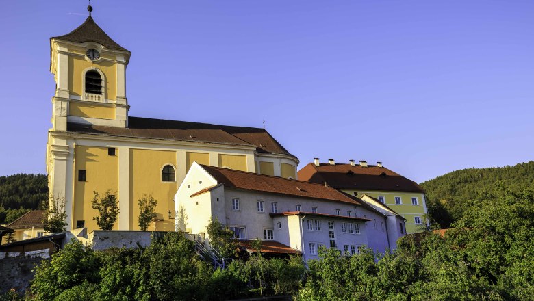 Pfarrkirche und Kloster in einer gr&uuml;nen Landschaft bei klarem Himmel.