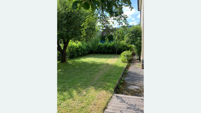 Ein gepflegter Garten mit Rasen, Bäumen und Sträuchern neben einem Haus.