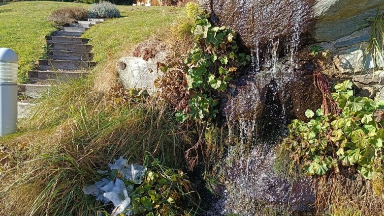 Kleiner Wasserfall in herbstlicher Landschaft mit B&auml;umen und blauem Himmel.