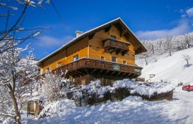 Ein Holzhaus im Schnee mit blauem Himmel im Hintergrund.