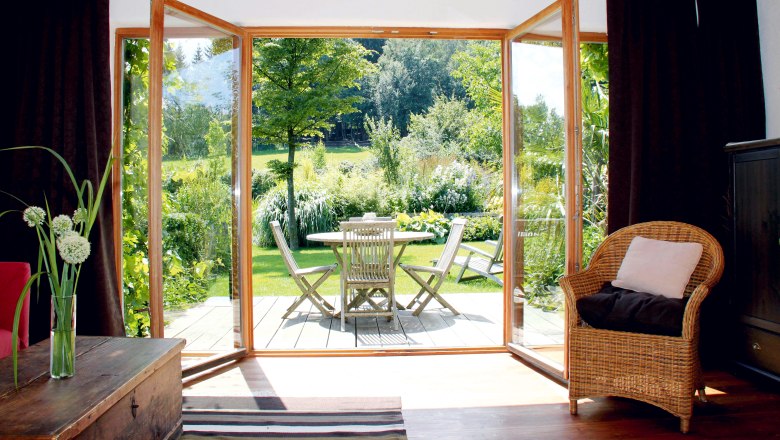Blick von einem Wohnzimmer auf eine Terrasse mit Gartenmöbeln und grünem Garten.