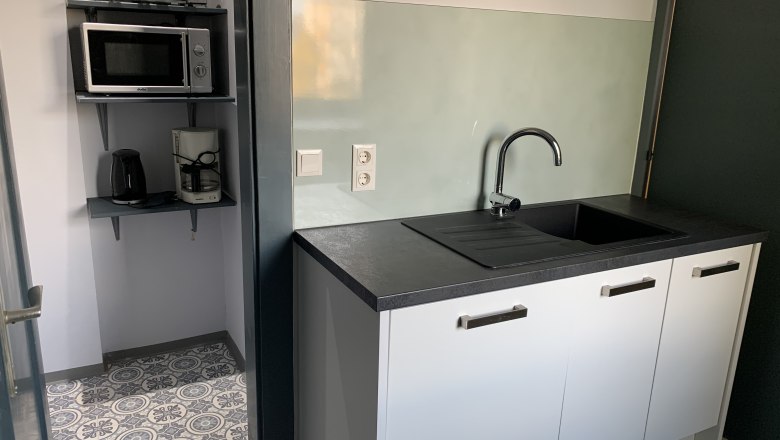 Kleine Küche mit Spüle, Mikrowelle, Toaster und Kaffeemaschine.