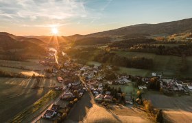 Luftaufnahme eines Dorfes in einer h&uuml;geligen Landschaft bei Sonnenuntergang.