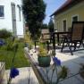 Terrasse mit Tisch, Stühlen und Pflanzen in einem Garten neben einem gelben Haus.