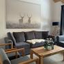 Wohnzimmer mit grauen Sofas, Holztisch und Hirschbild an der Wand.