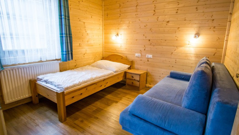 Kinderzimmer mit Holzw&auml;nden, Einzelbett, blauem Sofa und Nachttisch.