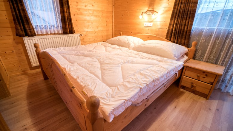 Gemütliches Schlafzimmer mit Holzwänden, Doppelbett und Nachttisch in einer Ferienwohnung.