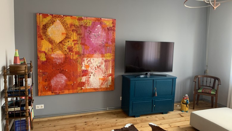 Wohnzimmer mit großem buntem Gemälde, Fernseher auf blauem Schrank, Holzboden und Kuhfell-Teppich.