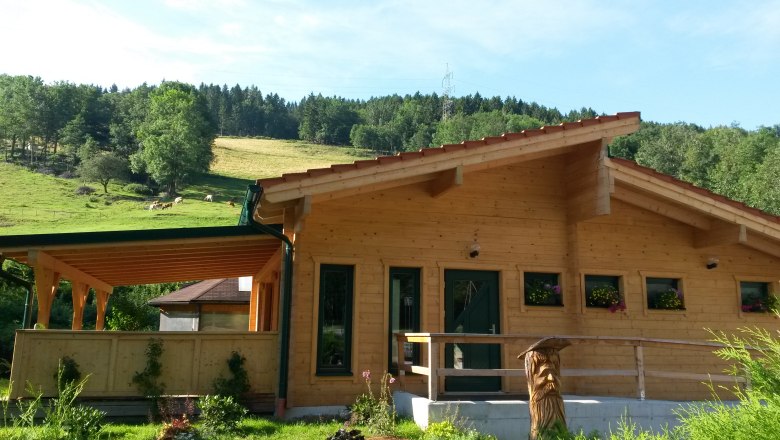Blockhaussauna in l&auml;ndlicher Umgebung mit Holzveranda und Blumenk&auml;sten.