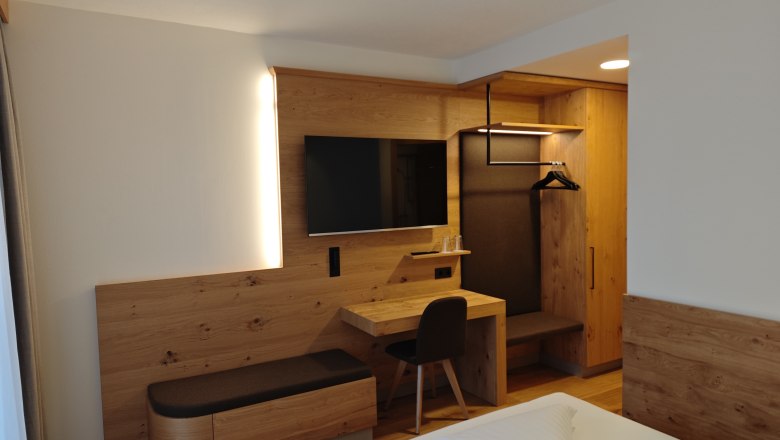 Modern eingerichtetes Hotelzimmer mit Holzm&ouml;beln, einem Schreibtisch, einem Fernseher und einem Kleiderschrank.