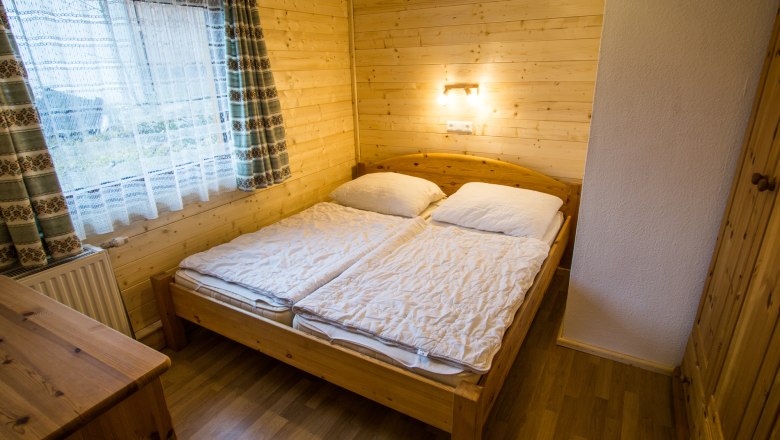 Gem&uuml;tliches Schlafzimmer mit Holzw&auml;nden, Doppelbett und Fenster mit Vorh&auml;ngen.